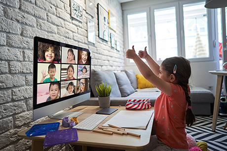 little girl making thumbs up in front of a monitor with video call